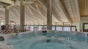 Ein großer, überdachter Schwimmbereich mit Holzbalken und Liegestühlen.