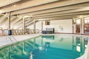 Una piscina interior con techo de madera, sillones de descanso y una sauna.
