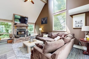 Una sala de estar con chimenea, un sofá, una mesa de centro y ventanas grandes.