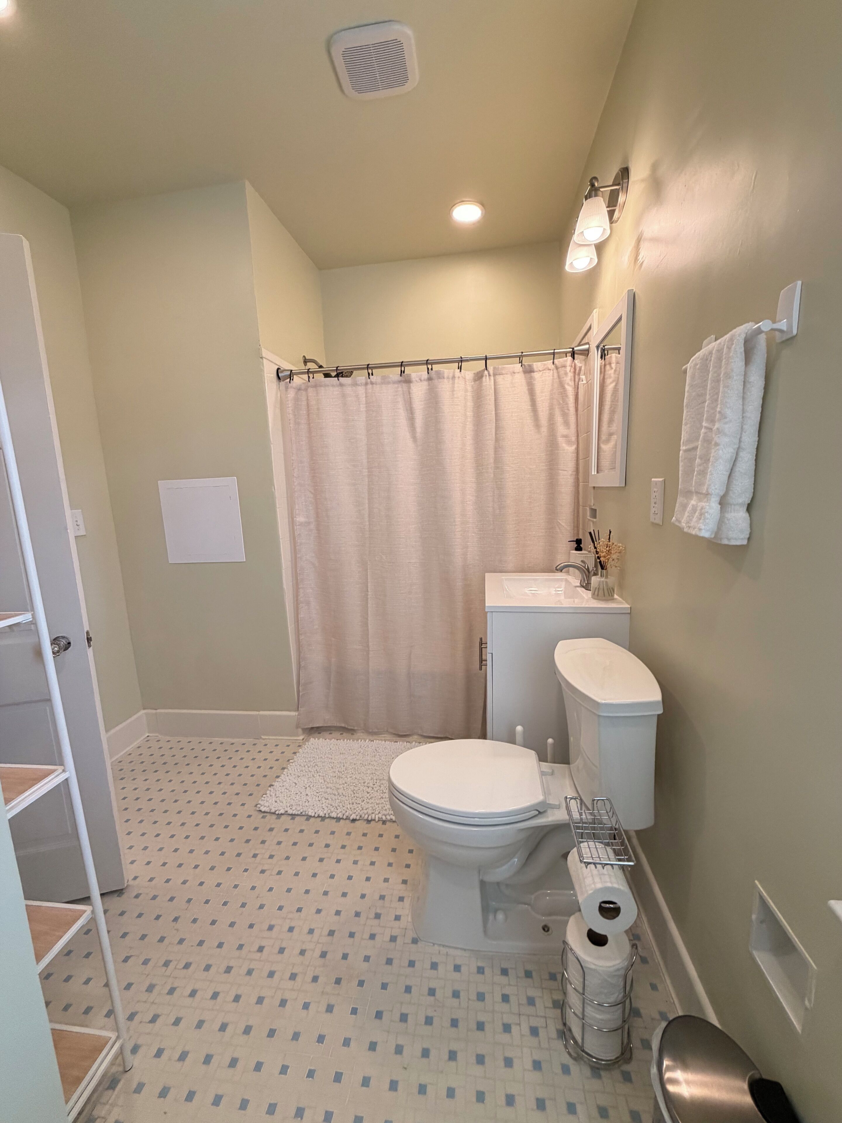 A bathroom with a toilet, sink, shower curtain, and a patterned floor.
