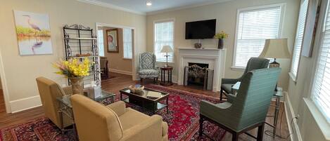 A living room with a fireplace, a television, a ceiling fan, and a patterned rug.