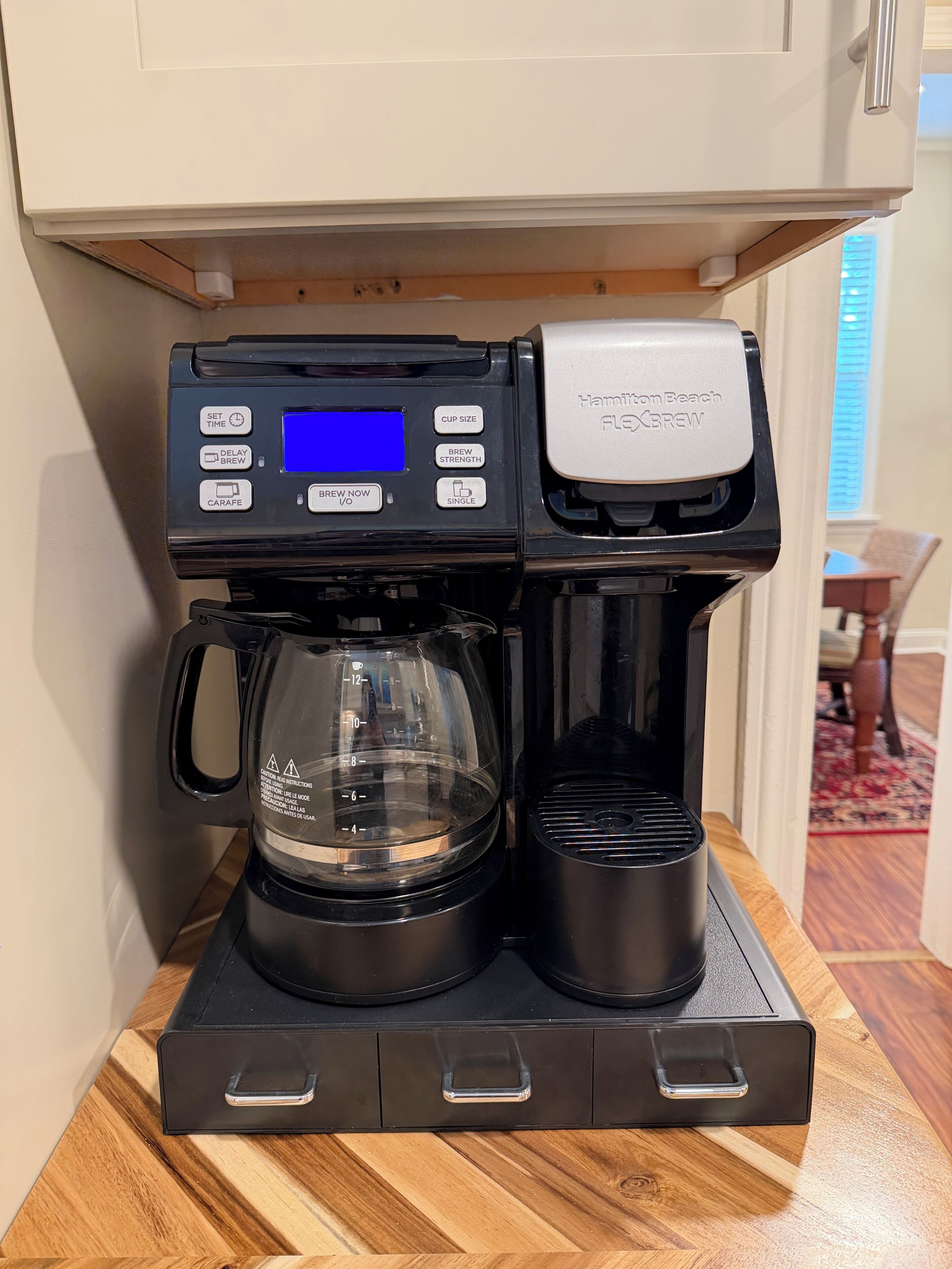 Una cafetera con pantalla digital, jarra y un solo portavasos sobre una encimera de madera.