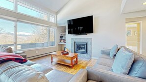 A spacious living room with a fireplace, a large TV mounted on the wall, and a sofa with cushions. - Mountain view retreat with fast WiFi, washer/dryer, & central AC (Jackson)