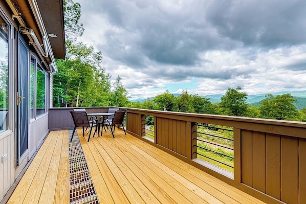 Eine Holzterrasse mit Tisch und Stühlen mit Blick auf eine gebirgige Landschaft.