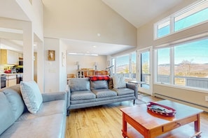 Ein geräumiges Wohnzimmer mit grauem Sofa, einem Holztisch und großen Fenstern mit Blick ins Freie.
