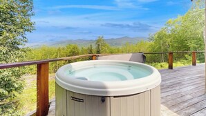 Un jacuzzi en una terraza de madera con vistas a montañas y árboles.