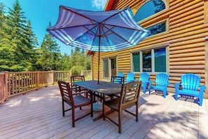 Eine Holzterrasse mit Tisch und Stühlen, einem blauen Sonnenschirm und Adirondack-Stühlen.