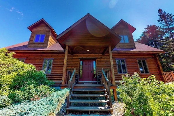 Eine Holzhütte mit einer Veranda, einer roten Tür und einer Treppe zum Eingang.