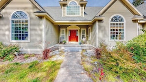 A two-story house with a central entrance, a covered porch, and a landscaped front yard. - Lovely home with water view, hot tub, fireplace, & washer/dryer (Conway)