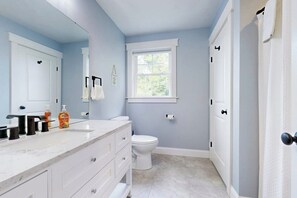 A bathroom with a white vanity, a toilet, a window, and a door. - Intervale home with mountain views and garage, central to Storyland (Bartlett)