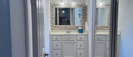 Un baño con un espejo grande, un tocador con cajones, un lavamanos y una alfombra azul en el suelo.