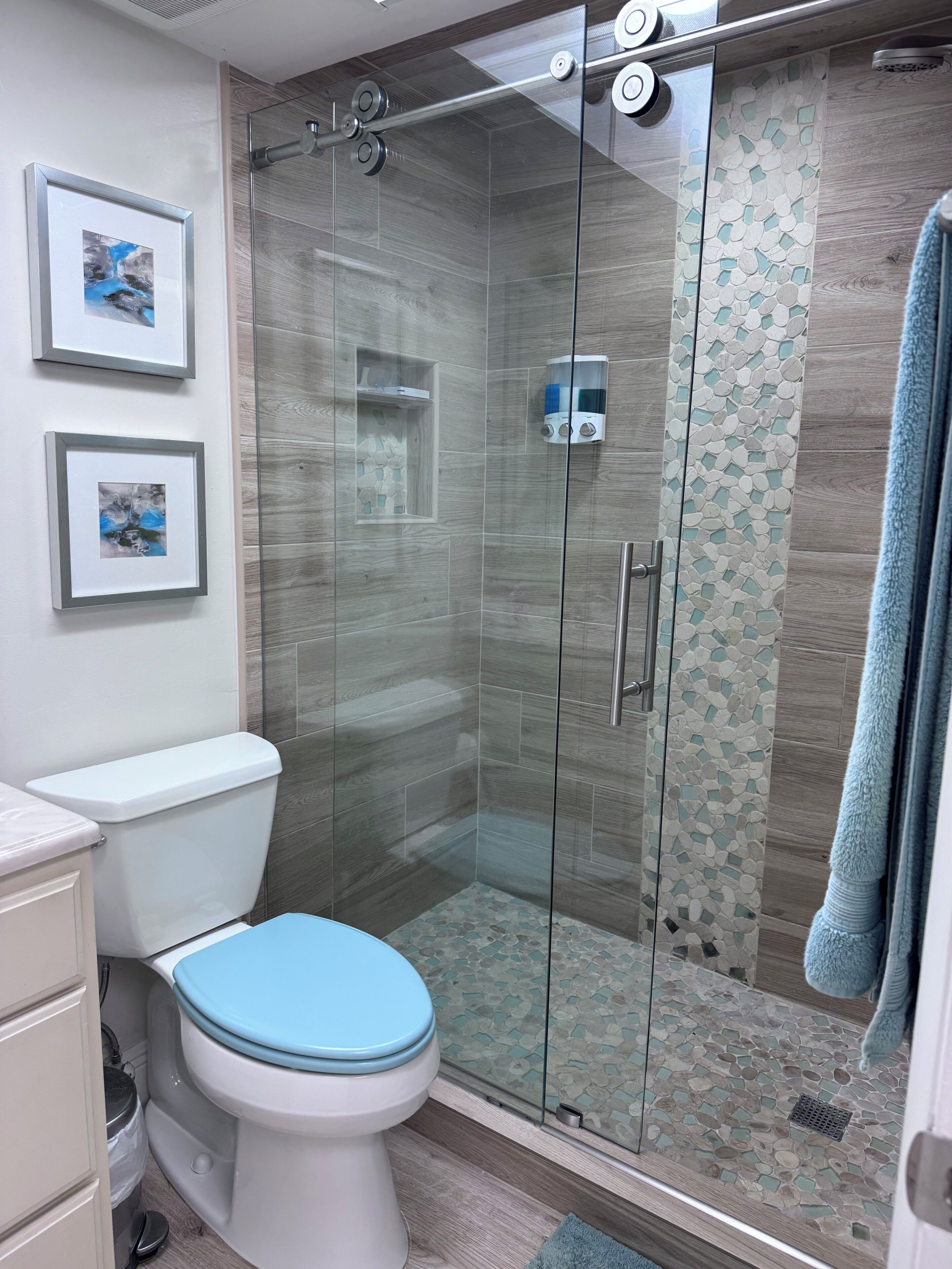 A bathroom with a toilet, a glass shower enclosure, and framed pictures on the wall.