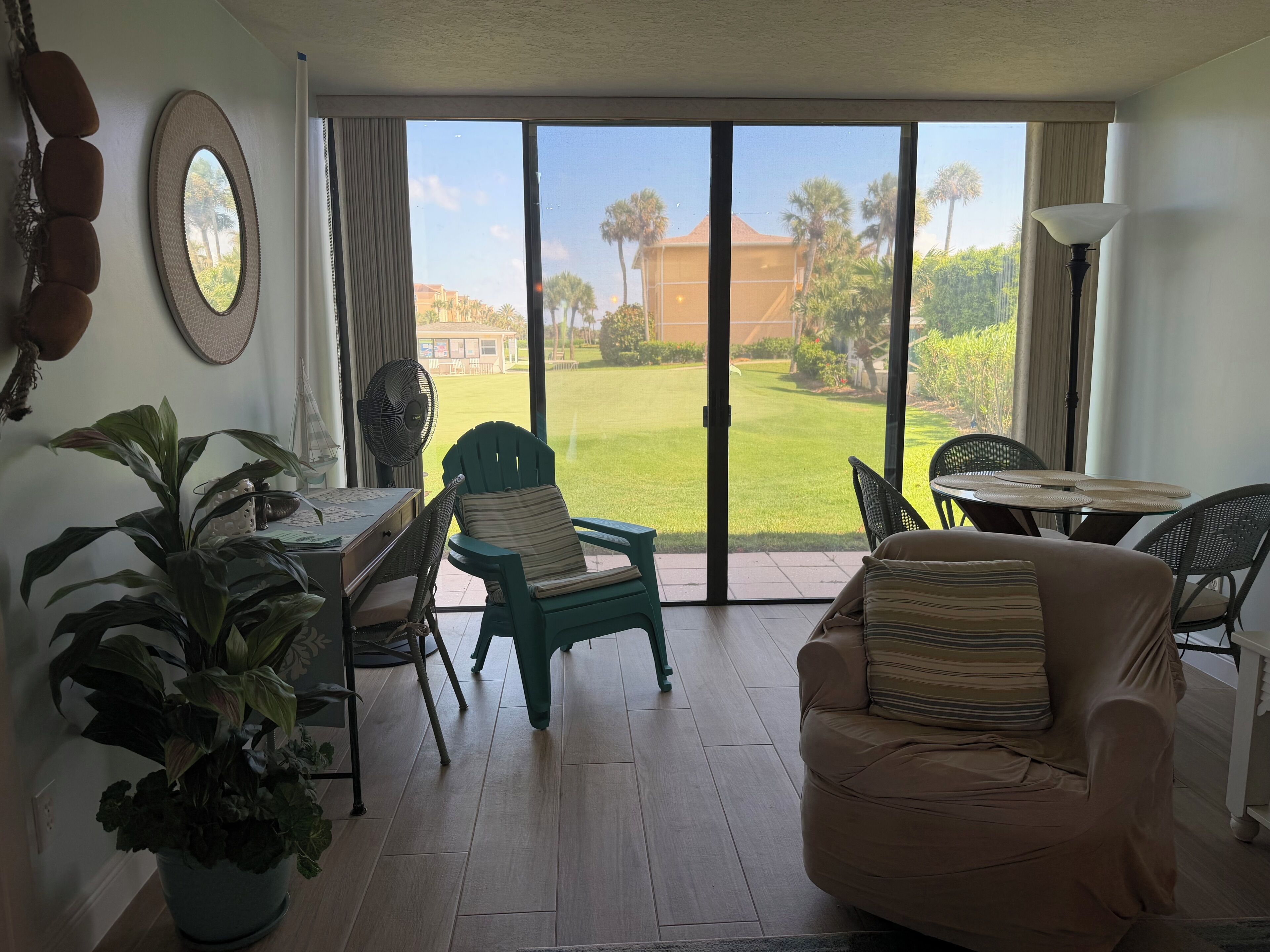 A room with a sliding glass door leading to a lawn, a dining table with chairs, a sofa, and a potted plant.