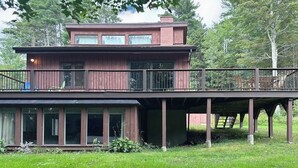 Ein zweistöckiges Holzhaus mit Balkon, großen Fenstern und einer überdachten Terrasse.