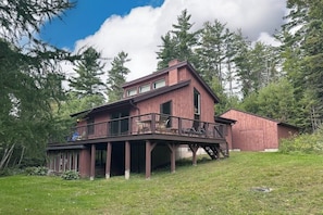 A two-story house with a deck, surrounded by trees.