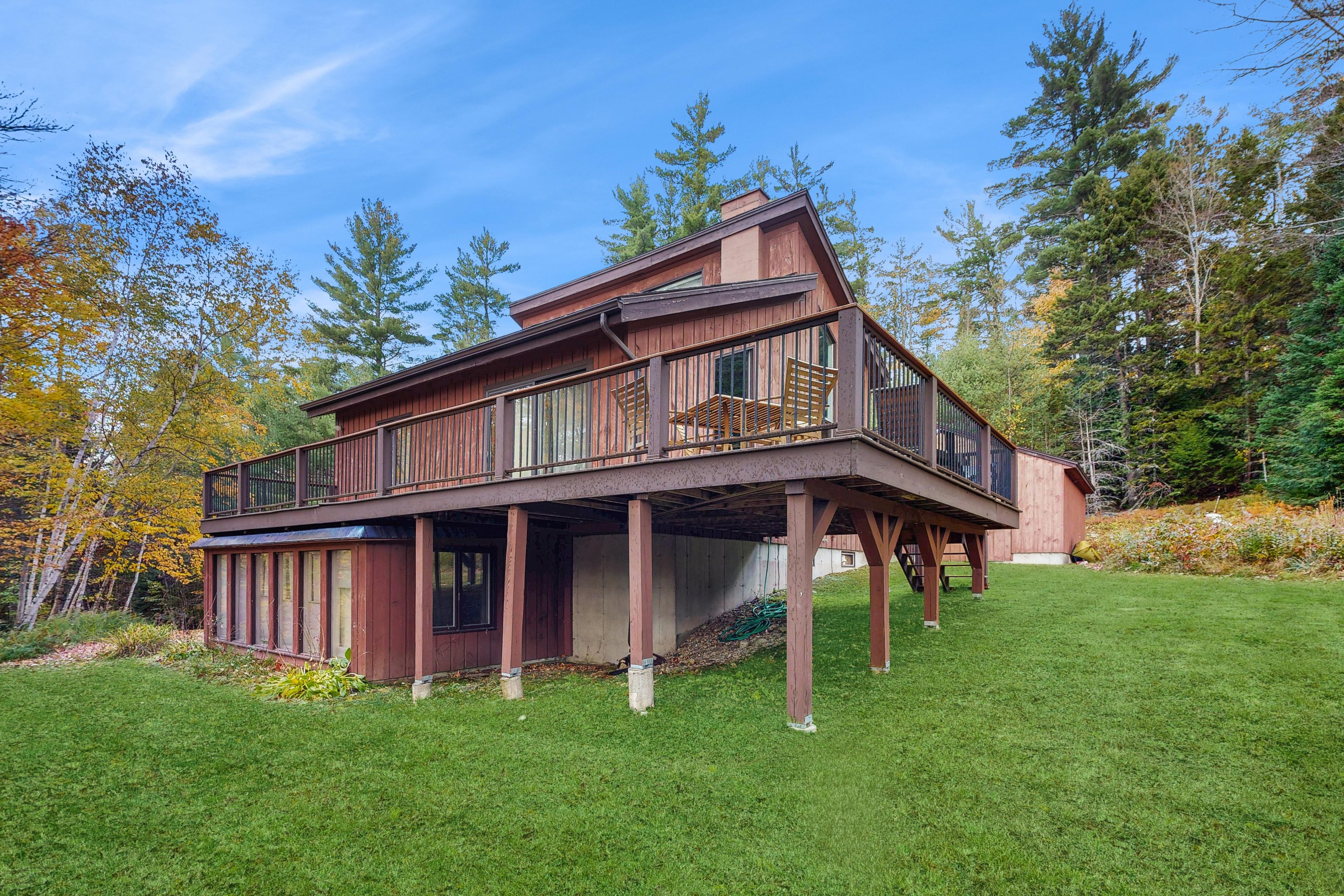 A two-story wooden house with a balcony, surrounded by a well-maintained lawn and trees.