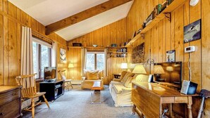 Ein gemütliches Blockhaus-Interieur mit Holzwänden, Kamin, Sofa, Schreibtisch und Fernseher.