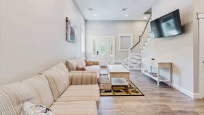Uma sala de estar com sofá, mesa de centro e televisão fixada na parede.