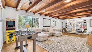 A spacious living room with a foosball table, a sofa, a large rug, and a bookshelf.