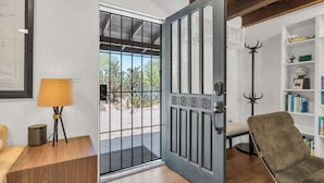 A room with a wooden floor, a sofa, a lamp, a bookshelf, and a door leading outside.