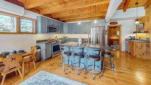 A kitchen with wooden ceiling beams, a central island with bar stools, and a dining area with wooden chairs. - Mittersill Village Gem  | House in Franconia with balcony, fireplace, & dogs ok (Franconia)