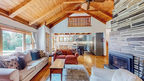 A spacious living area with a high ceiling, wooden beams, a stone fireplace, and a kitchen in the background. - Mittersill Village Gem  | House in Franconia with balcony, fireplace, & dogs ok (Franconia)