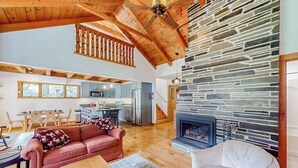 A spacious living area with a stone fireplace, wooden ceiling beams, and a kitchen in the background. - Mittersill Village Gem  | House in Franconia with balcony, fireplace, & dogs ok (Franconia)