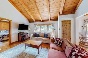 Ein gemütliches Wohnzimmer mit Holzboden, einer Couch, einem Couchtisch und einem Fernseher.