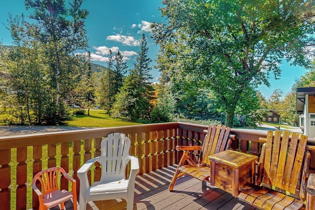 A deck with wooden chairs and a table, overlooking a green landscape with trees and a distant building.