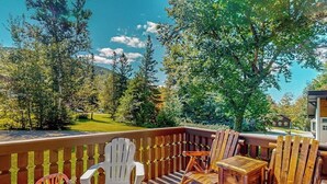 A deck with wooden chairs and a table, overlooking a green landscape with trees and a distant building. - Mittersill Village Gem  | House in Franconia with balcony, fireplace, & dogs ok (Franconia)