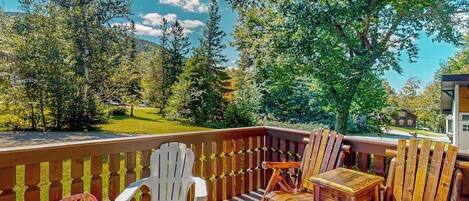 A deck with wooden chairs and a table, overlooking a green landscape with trees and a distant building.