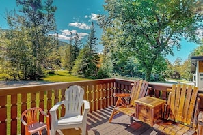 Eine Terrasse mit Holzkästen und Tisch, mit Blick auf eine grüne Landschaft mit Bäumen und einem entfernten Gebäude.