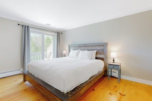 A bedroom with a wooden bed, a nightstand with a lamp, and a view of the outdoors through a large window. - Mountain view condo with gas fireplace, balcony, & grill - close to skiing (Jackson)