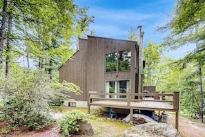 Eine moderne Holzhütte mit einer Terrasse, umgeben von Bäumen.