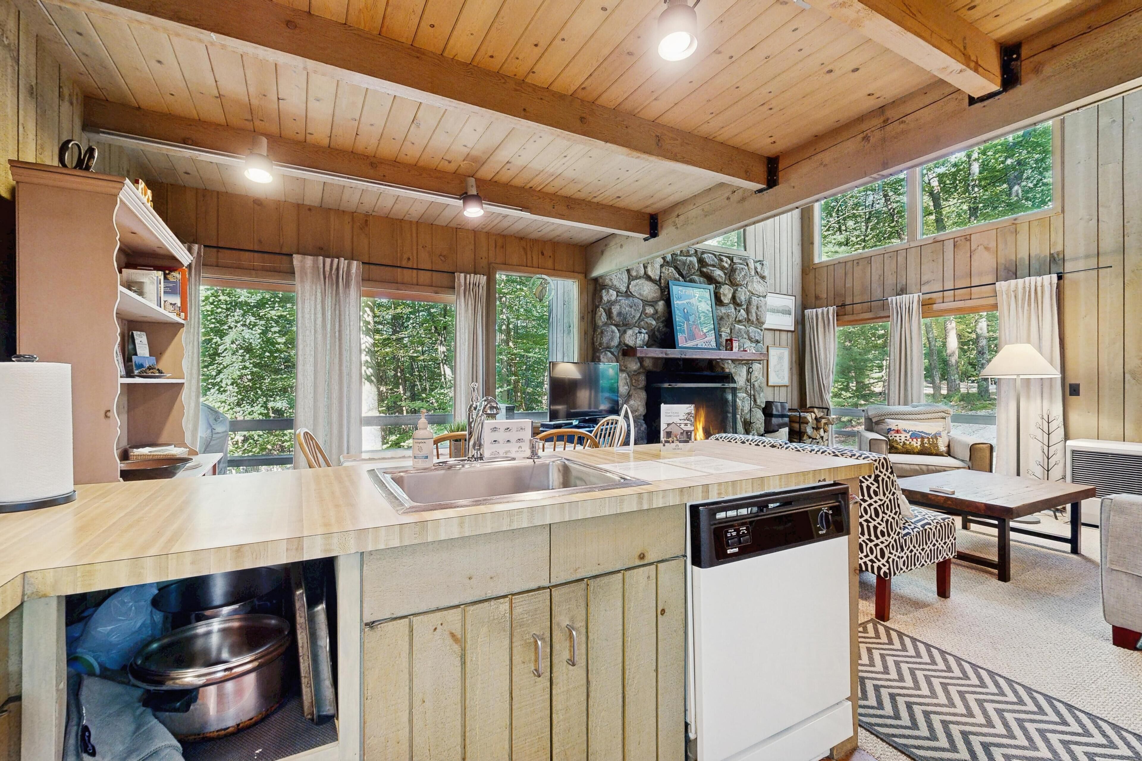 A spacious kitchen with a stone fireplace, wooden ceiling, and large windows offering a view of the outdoors.