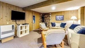 Ein Zimmer mit Holzwänden, einem Kamin, einem Flachbildfernseher, einer Couch und einer Lampe.