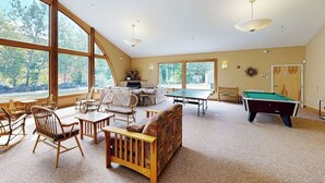 Een ruime kamer met een pooltafel, een biljarttafel en nog een pooltafel. Er zijn meerdere houten stoelen en een bank.