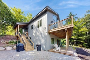 Ein zweistöckiges Haus mit einer Holzterrasse, einer Treppe und einem überdachten Sitzbereich im Freien.