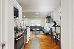 A compact kitchen with a stove, oven, and dining area with a sofa and bar stools.