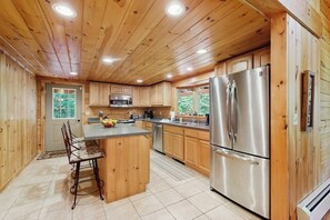 Cocina de cabaña de madera con una isla central, electrodomésticos de acero inoxidable y vista a zonas verdes.