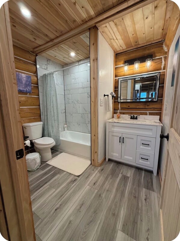 A wooden-paneled bathroom with a toilet, bathtub, and vanity.