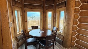 L’intérieur d’une cabane en rondins, avec une table et des chaises en bois rond, de grandes fenêtres et une vue sur le désert.