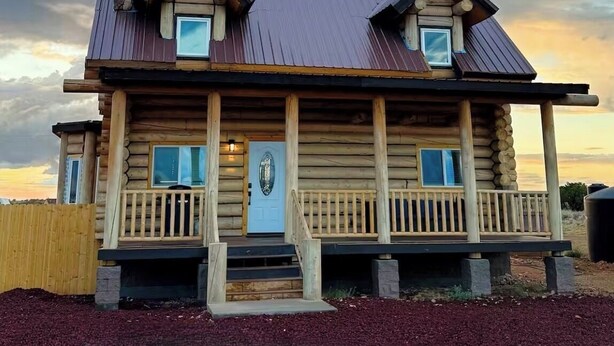 Une cabane en rondins à deux étages, dotée d’un porche, d’une cheminée en pierre et offrant une vue sur le ciel.