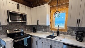 Une cuisine moderne avec des armoires blanches, des appareils en acier inoxydable, un plafond en bois et une fenêtre offrant une belle vue.