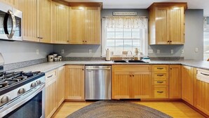 Una cocina con armarios de madera, lavavajillas de acero inoxidable y cocina a gas.