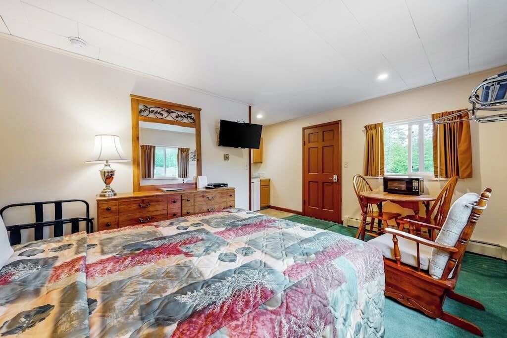 A bedroom with a bed, dresser, TV, and a dining area with chairs.
