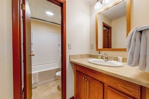 A bathroom with a white toilet, a bathtub, a sink with a mirror above it, and wooden cabinets. - Charming and casual motel in a great location with shared resort amenities (Lincoln)