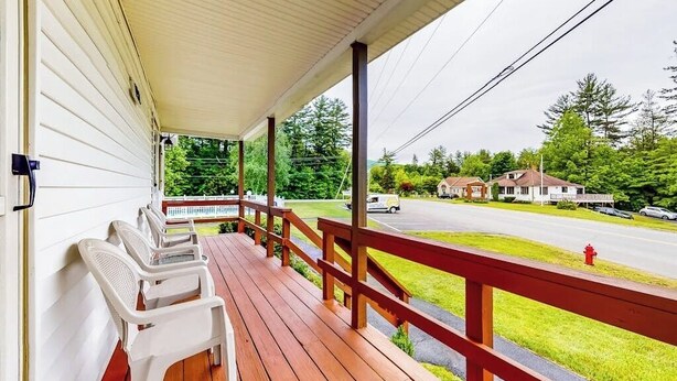 A covered porch with wooden flooring and a red railing, overlooking a street with houses and a fire hydrant. - Charming and casual motel in a great location with shared resort amenities (Lincoln)