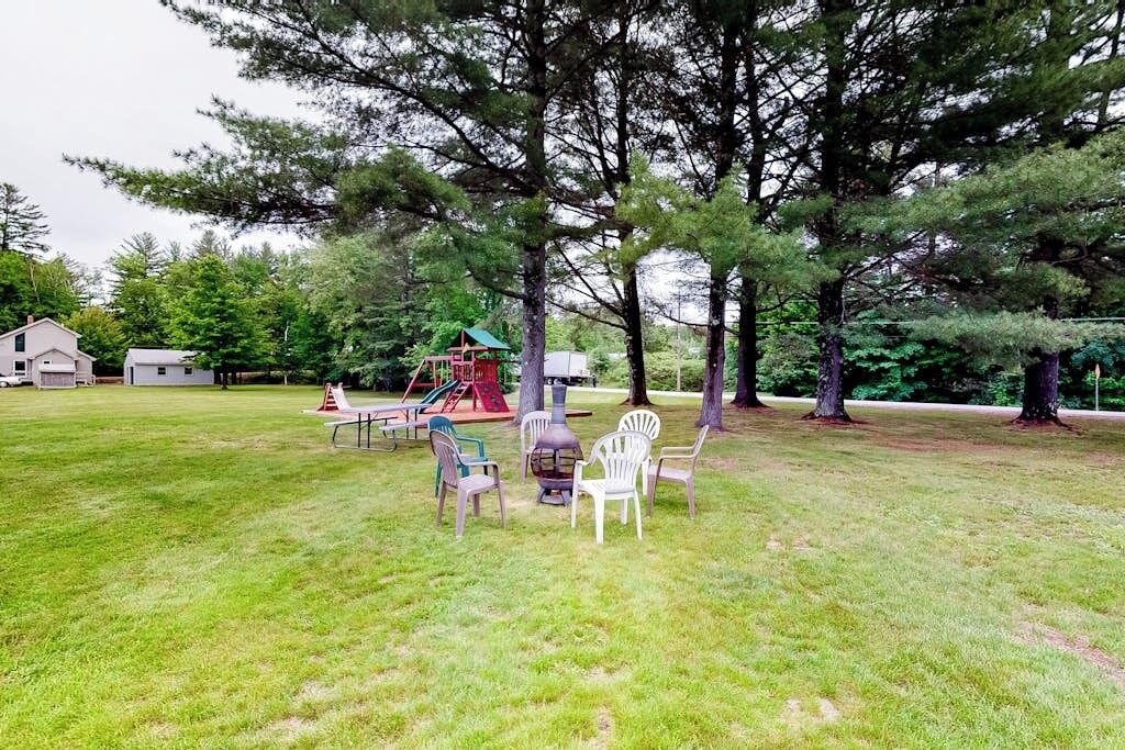 A grassy outdoor area with a playground, chairs, and a picnic table.