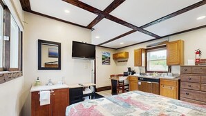 Un dormitorio con cama, escritorio, silla, televisión, armarios de madera, ventana y extintor.